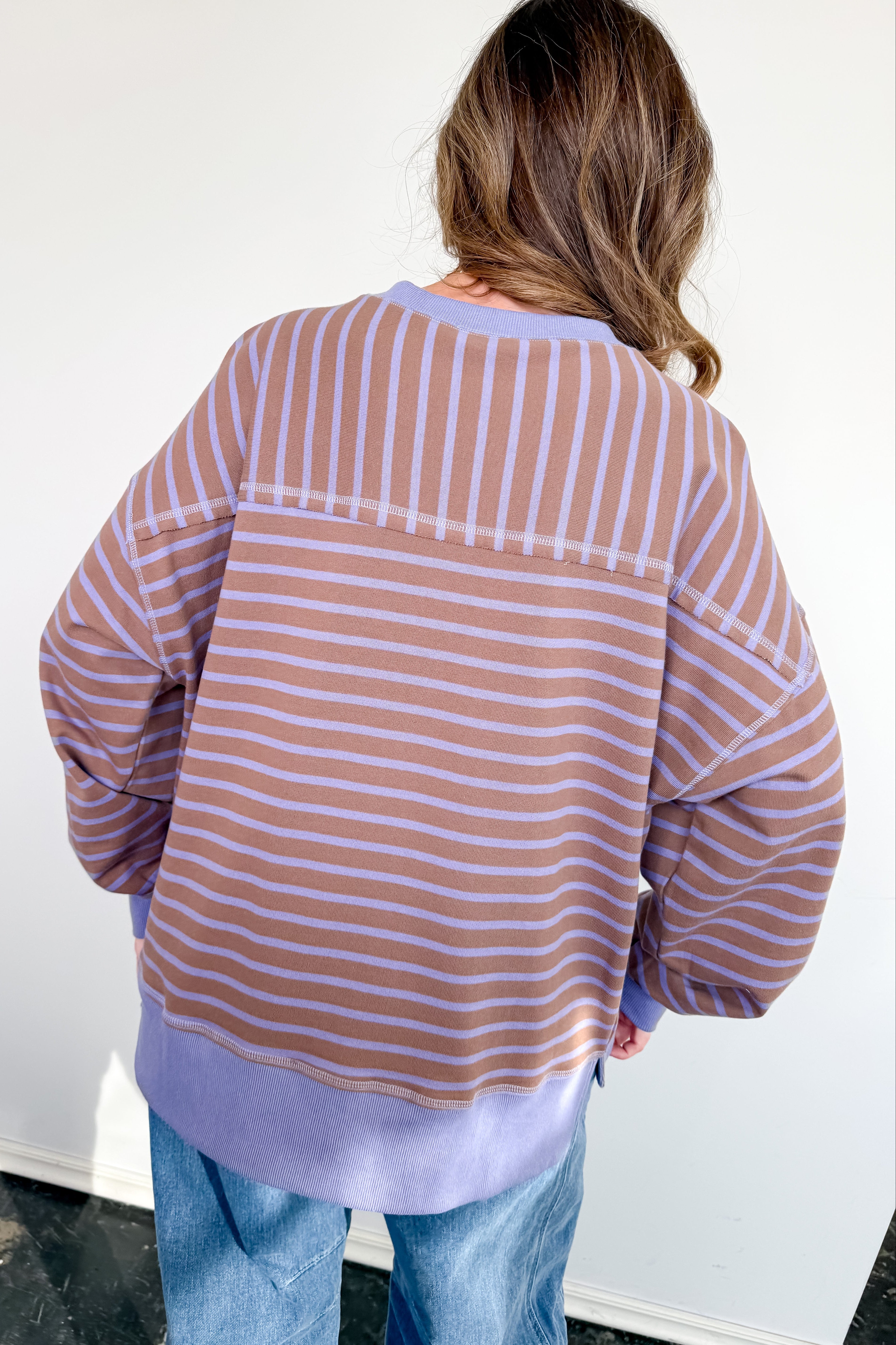 Person wearing a striped shirt and jeans against a white wall