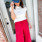 Person wearing a blue cap, white shirt, and red pants standing in front of a door.