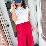 Person wearing a blue cap, white shirt, and red pants standing in front of a door.