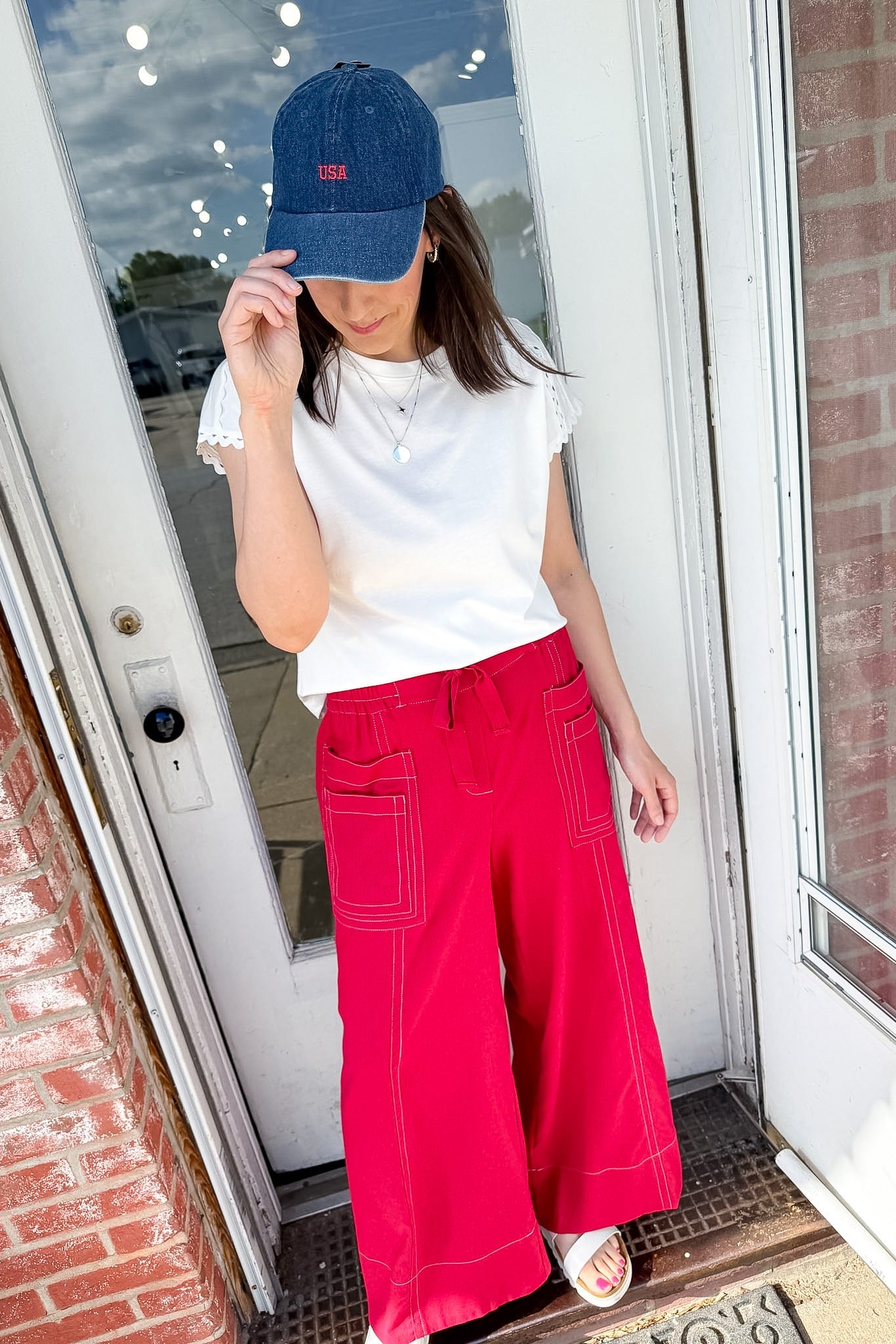 Person wearing a blue cap, white shirt, and red pants standing in front of a door.