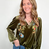 Woman wearing a green velvet top with floral embroidery against a white background