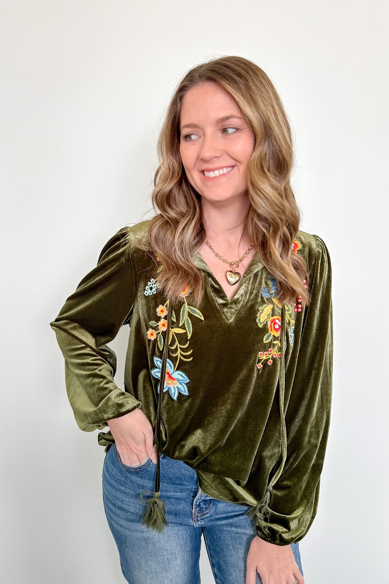 Woman wearing a green velvet top with floral embroidery against a white background