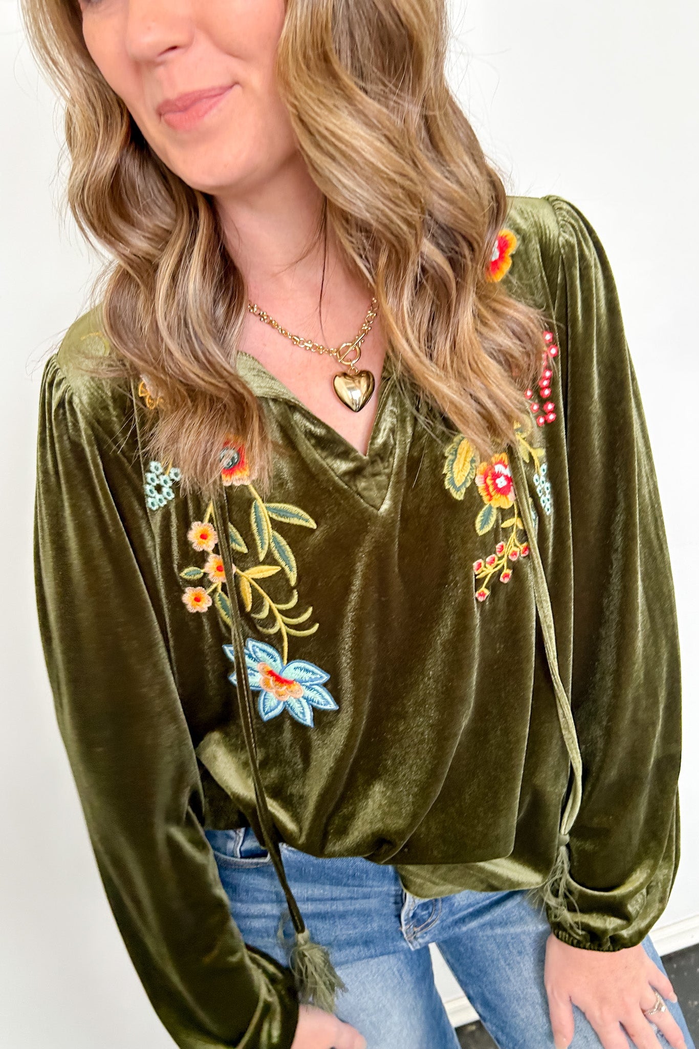 Woman wearing an olive green velvet blouse with floral embroidery on a white background