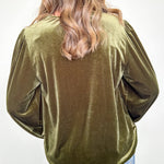 Person wearing an olive green velvet top with long sleeves against a white background