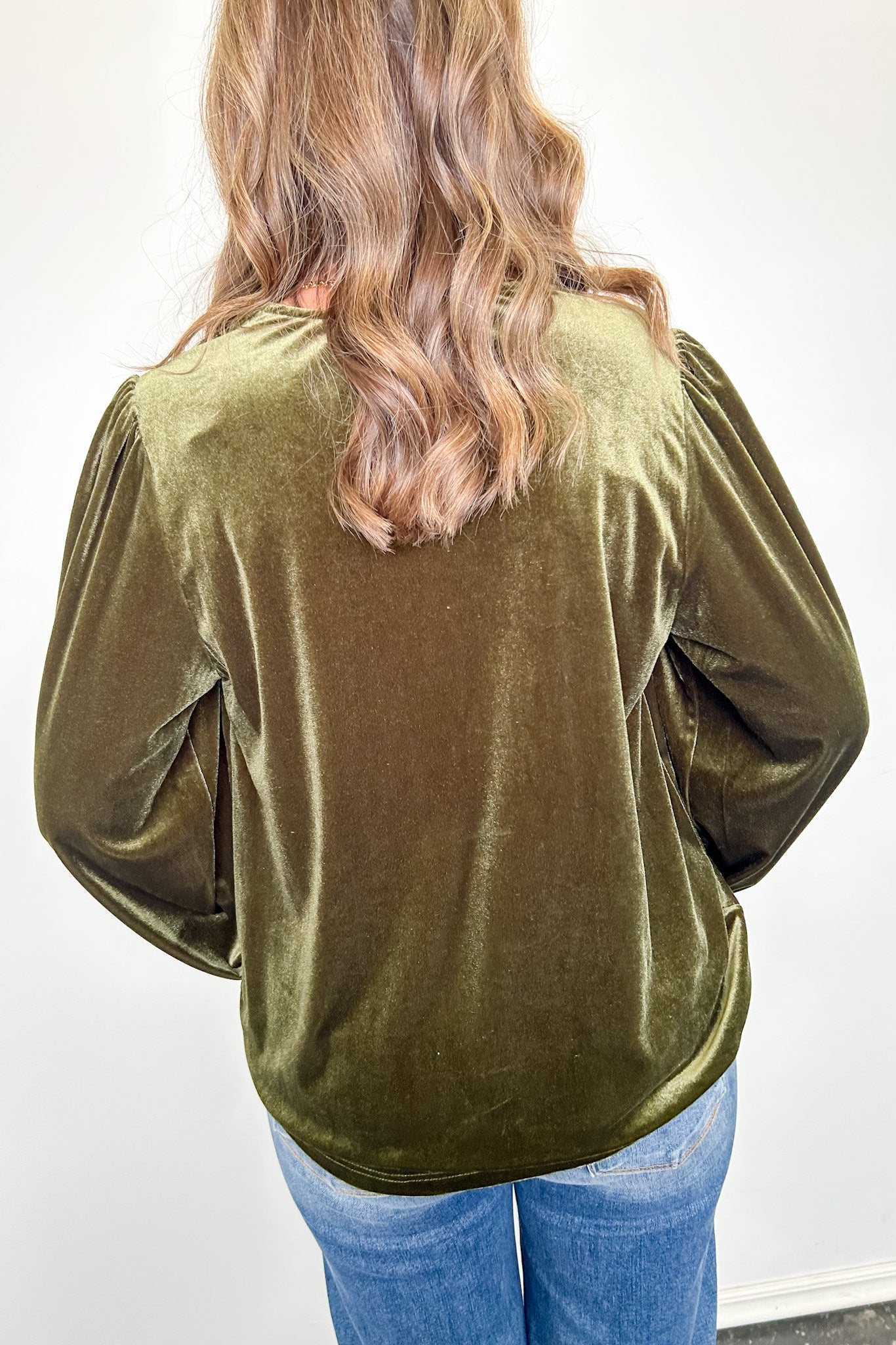 Person wearing an olive green velvet top with long sleeves against a white background