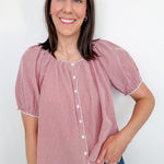 A woman wearing a red and white puff sleeve top standing in front of a white wall.