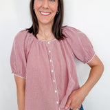 A woman wearing a red and white puff sleeve top standing in front of a white wall.