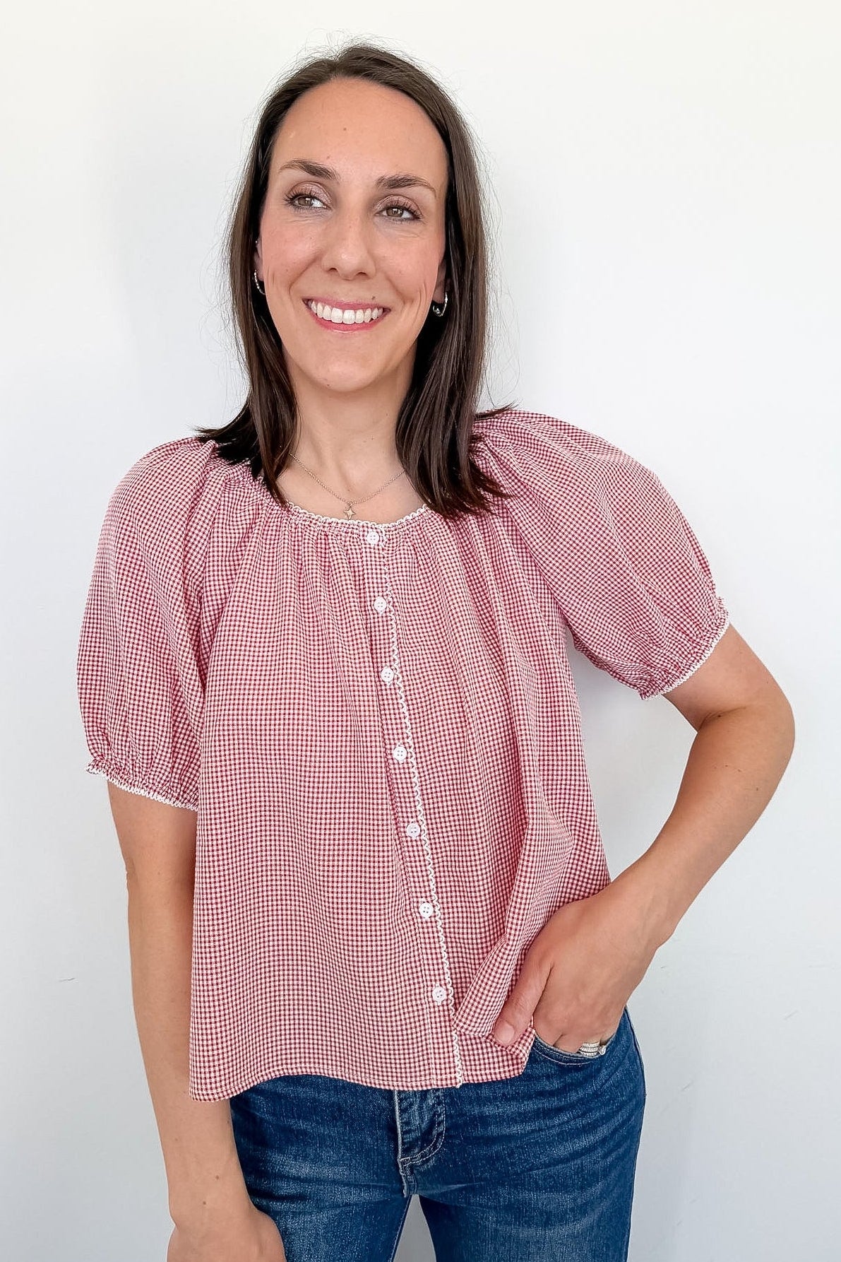 A woman wearing a red and white puff sleeve top standing in front of a white wall.