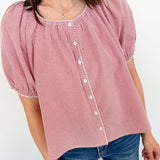 Person wearing a red and white checkered blouse with puffed sleeves against a white background