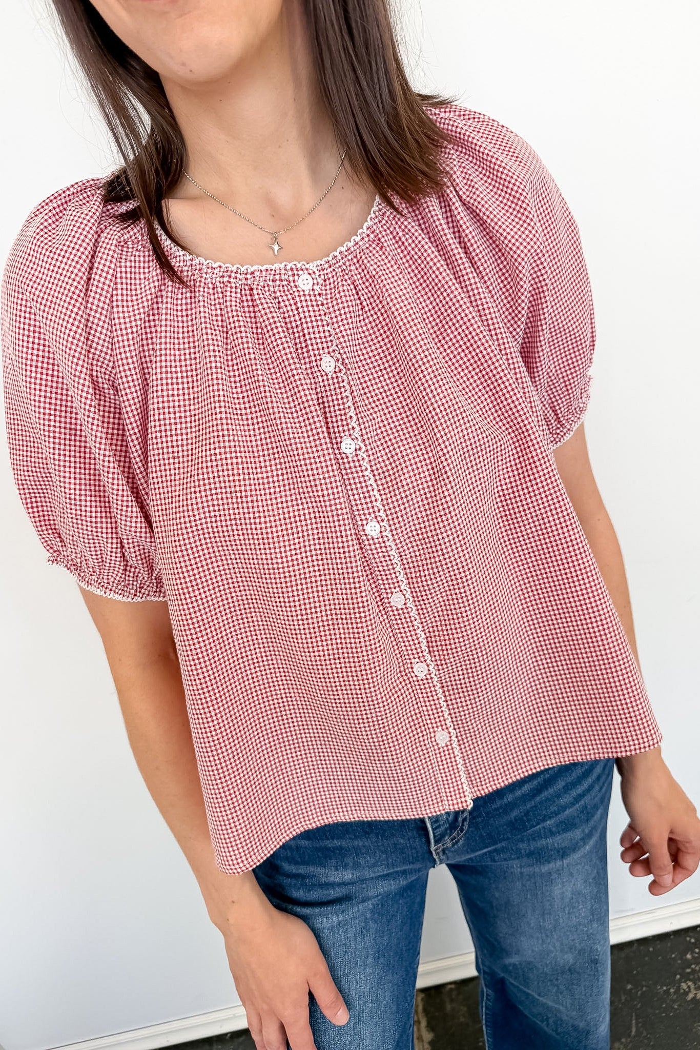 Person wearing a red and white checkered blouse with puffed sleeves against a white background