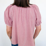Person wearing a pink checkered blouse with puffed sleeves against a white wall.