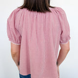 Person wearing a pink checkered blouse with puffed sleeves against a white wall.