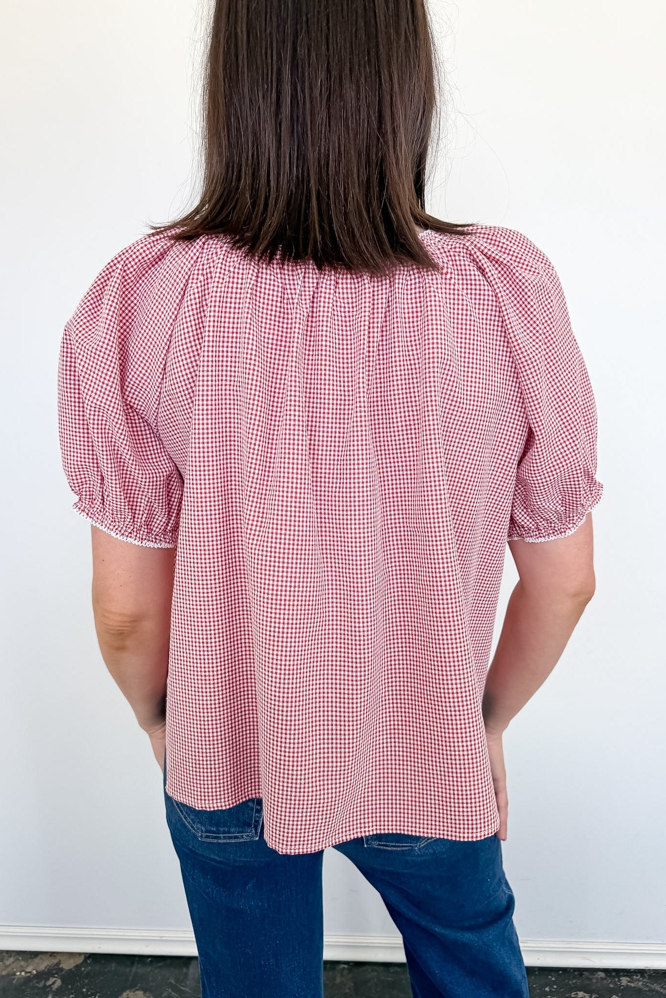 Person wearing a pink checkered blouse with puffed sleeves against a white wall.