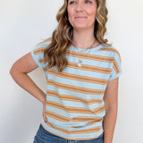 Woman wearing a light blue and orange striped shirt with jeans against a white background