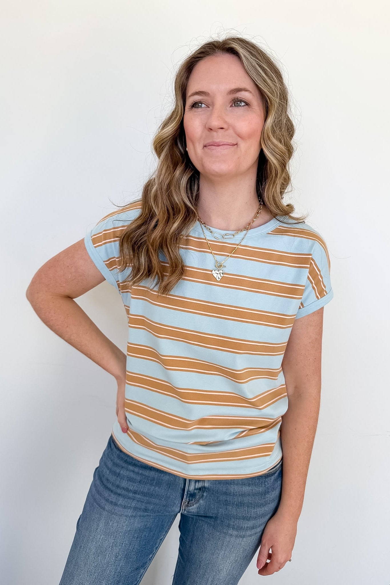 Woman wearing a light blue and orange striped shirt with jeans against a white background