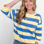 Woman wearing a yellow and blue striped sweater with sunglasses on her head against a white background