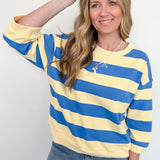 Woman wearing a yellow and blue striped sweater with sunglasses on her head against a white background