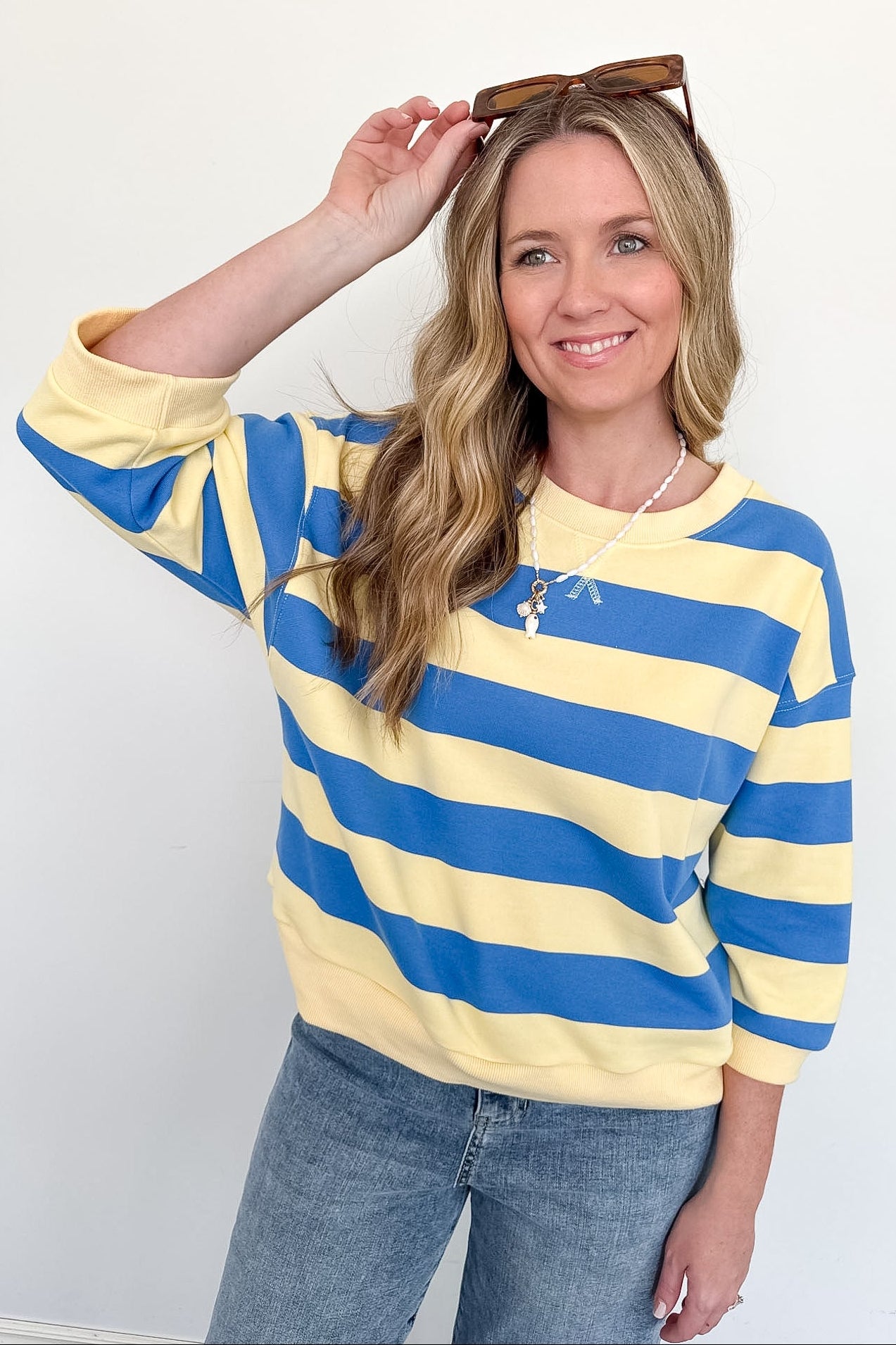 Woman wearing a yellow and blue striped sweater with sunglasses on her head against a white background