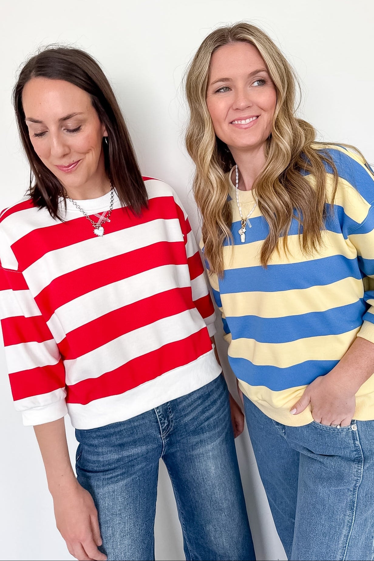 Two women wearing colorful striped sweaters against a white background