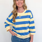 Woman wearing a blue and yellow striped sweater with sunglasses on her head against a white background