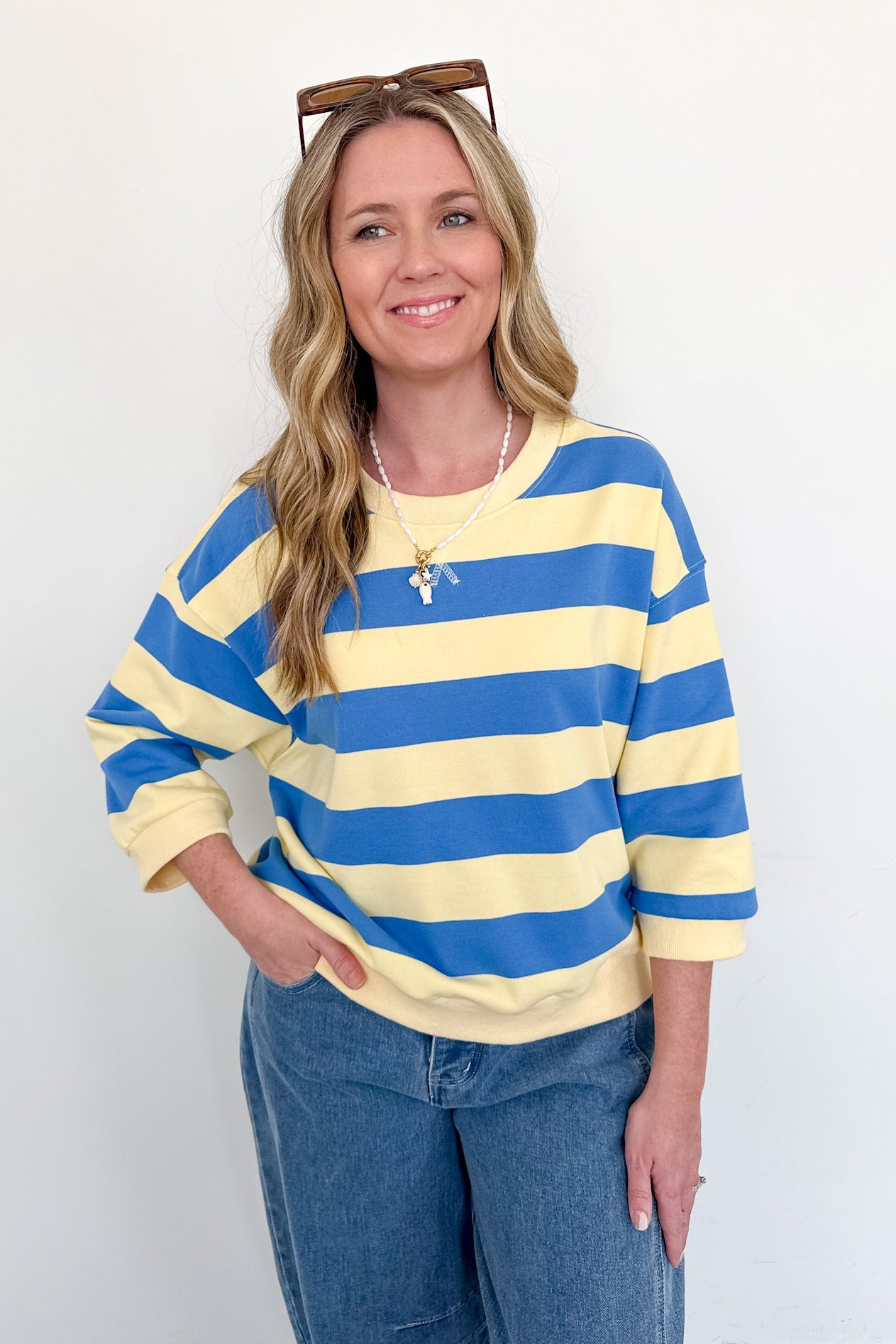 Woman wearing a blue and yellow striped sweater with sunglasses on her head against a white background