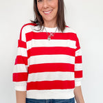 A woman wearing a red and white striped shirt that is standing in front of a white wall.