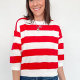 A woman wearing a red and white striped shirt that is standing in front of a white wall.