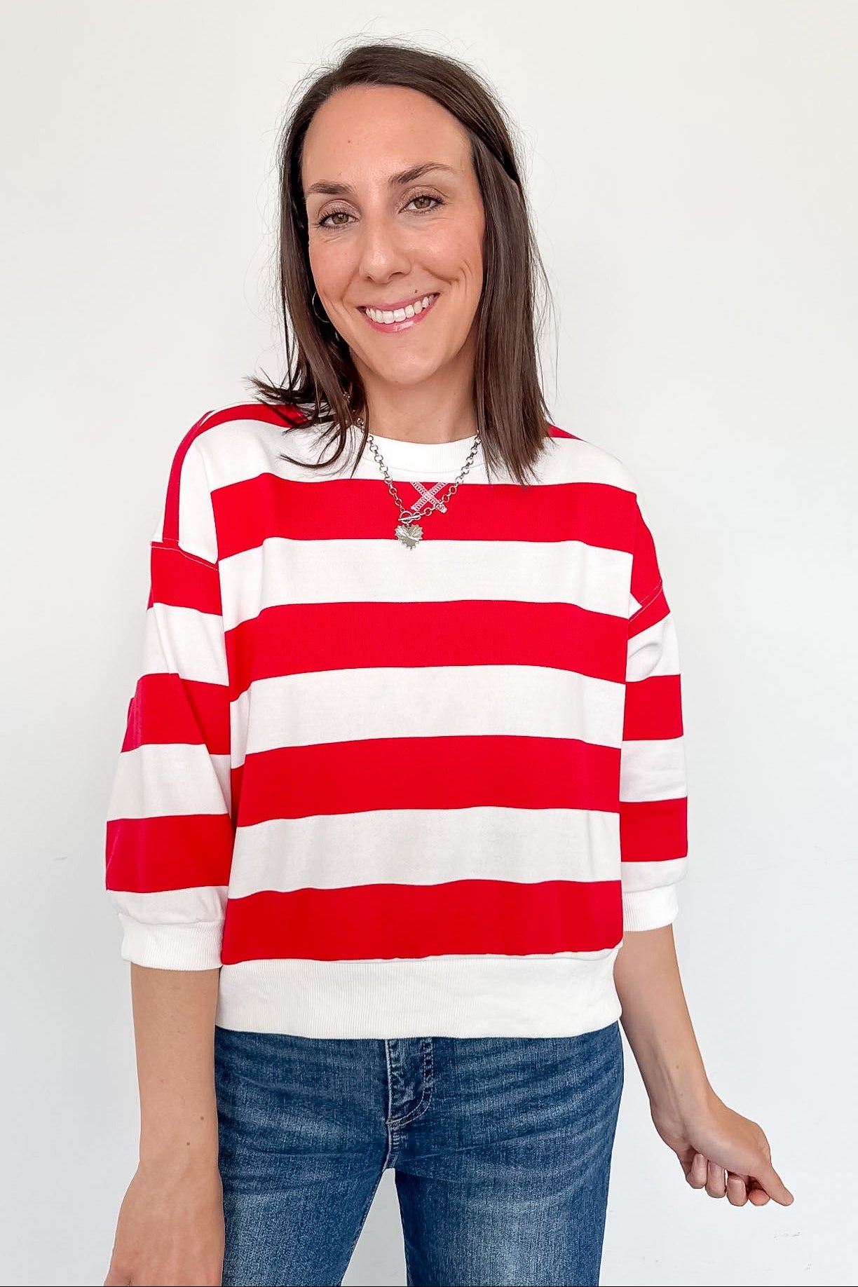 A woman wearing a red and white striped shirt that is standing in front of a white wall.