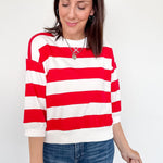 A woman wearing a red and white 3/4 length sleeve top with jeans.