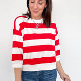 A woman wearing a red and white 3/4 length sleeve top with jeans.