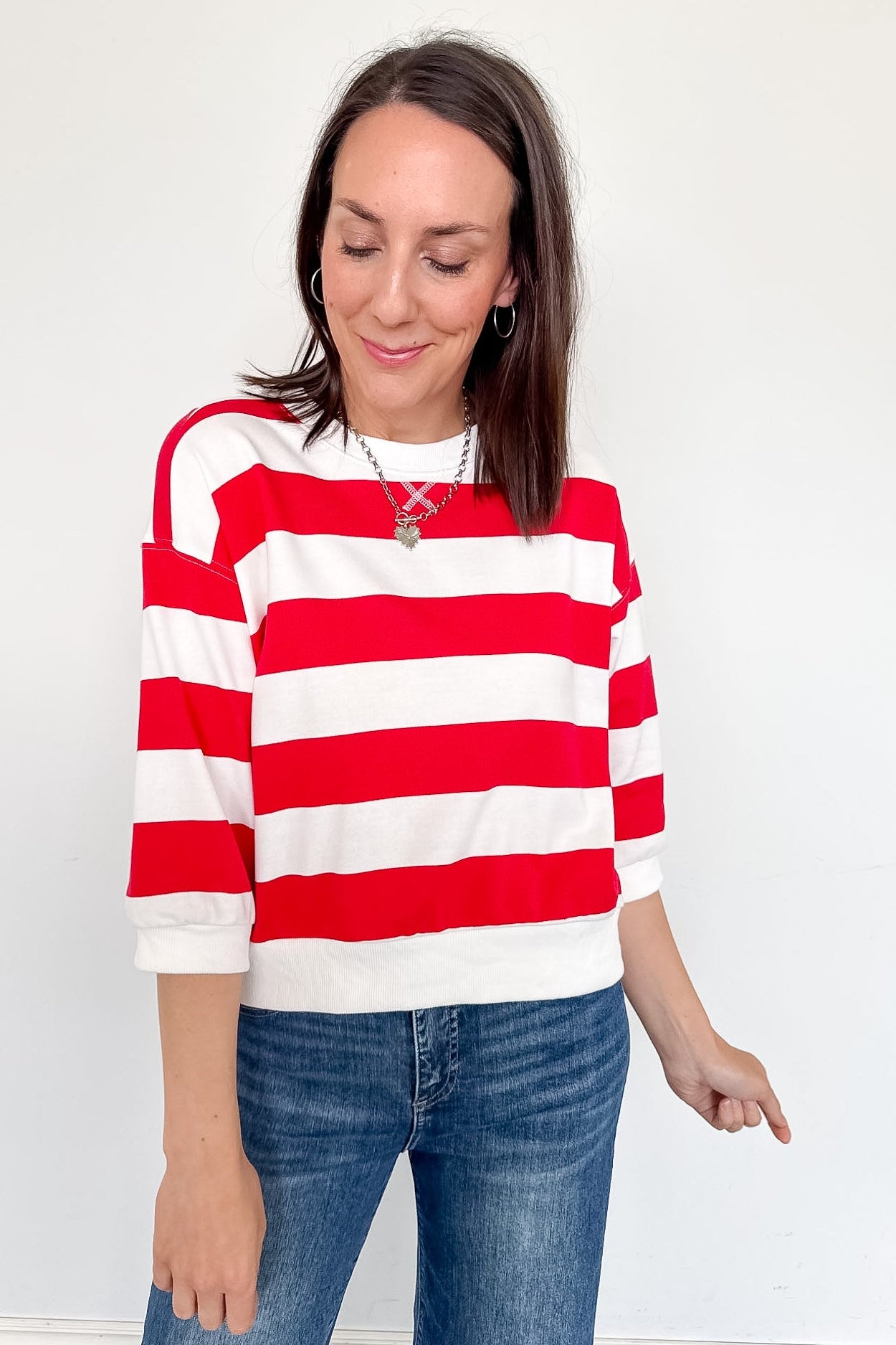 A woman wearing a red and white 3/4 length sleeve top with jeans.