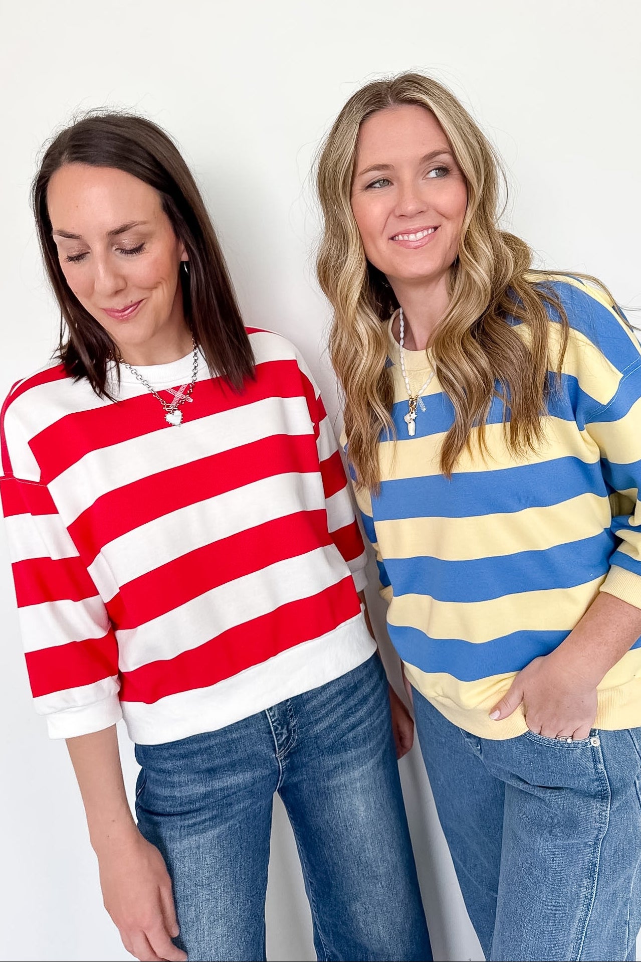 Two women wearing colorful striped sweaters against a white background