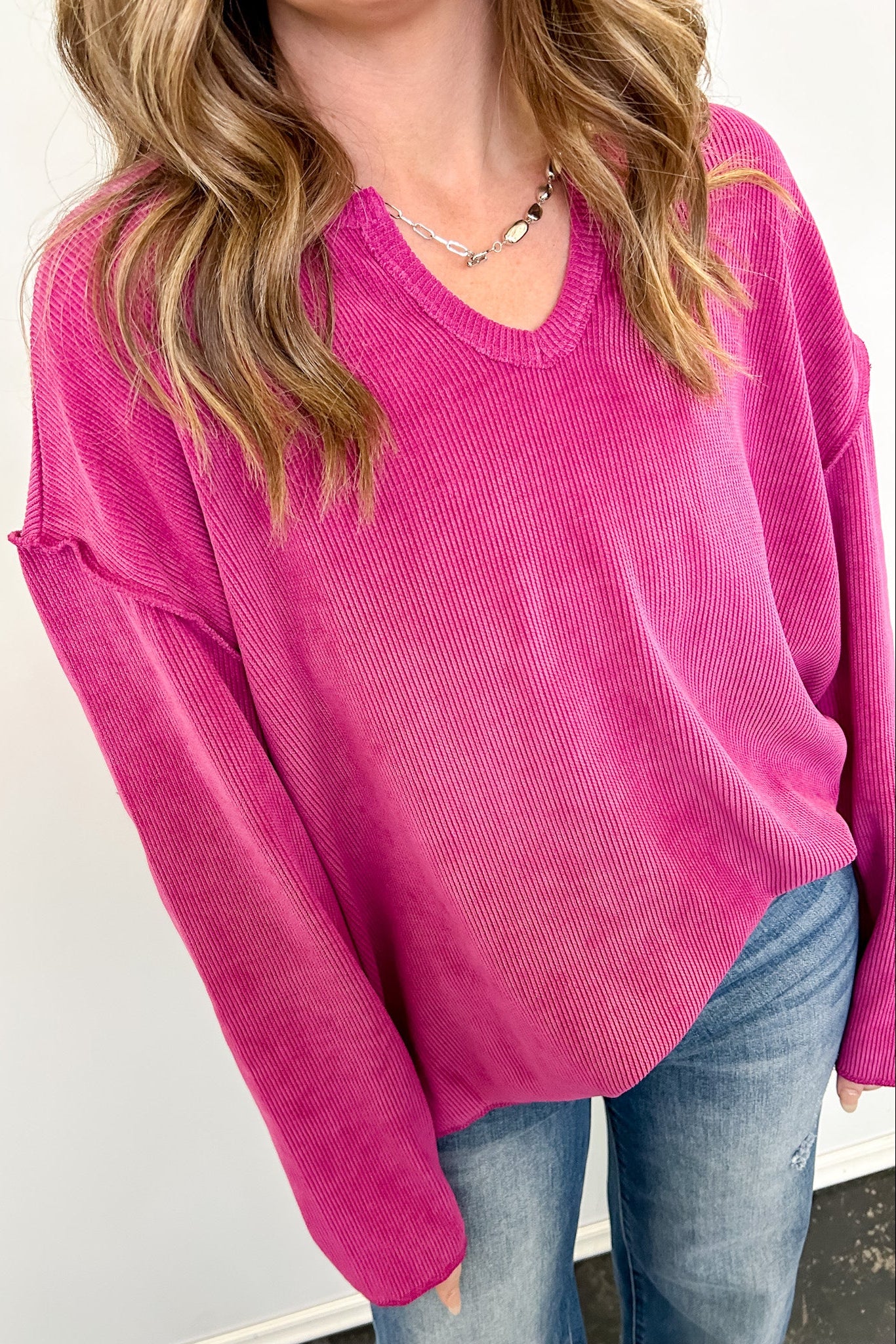 Person wearing a bright pink sweater and blue jeans against a white background