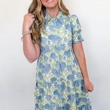 Woman wearing a blue and green floral dress against a white wall.
