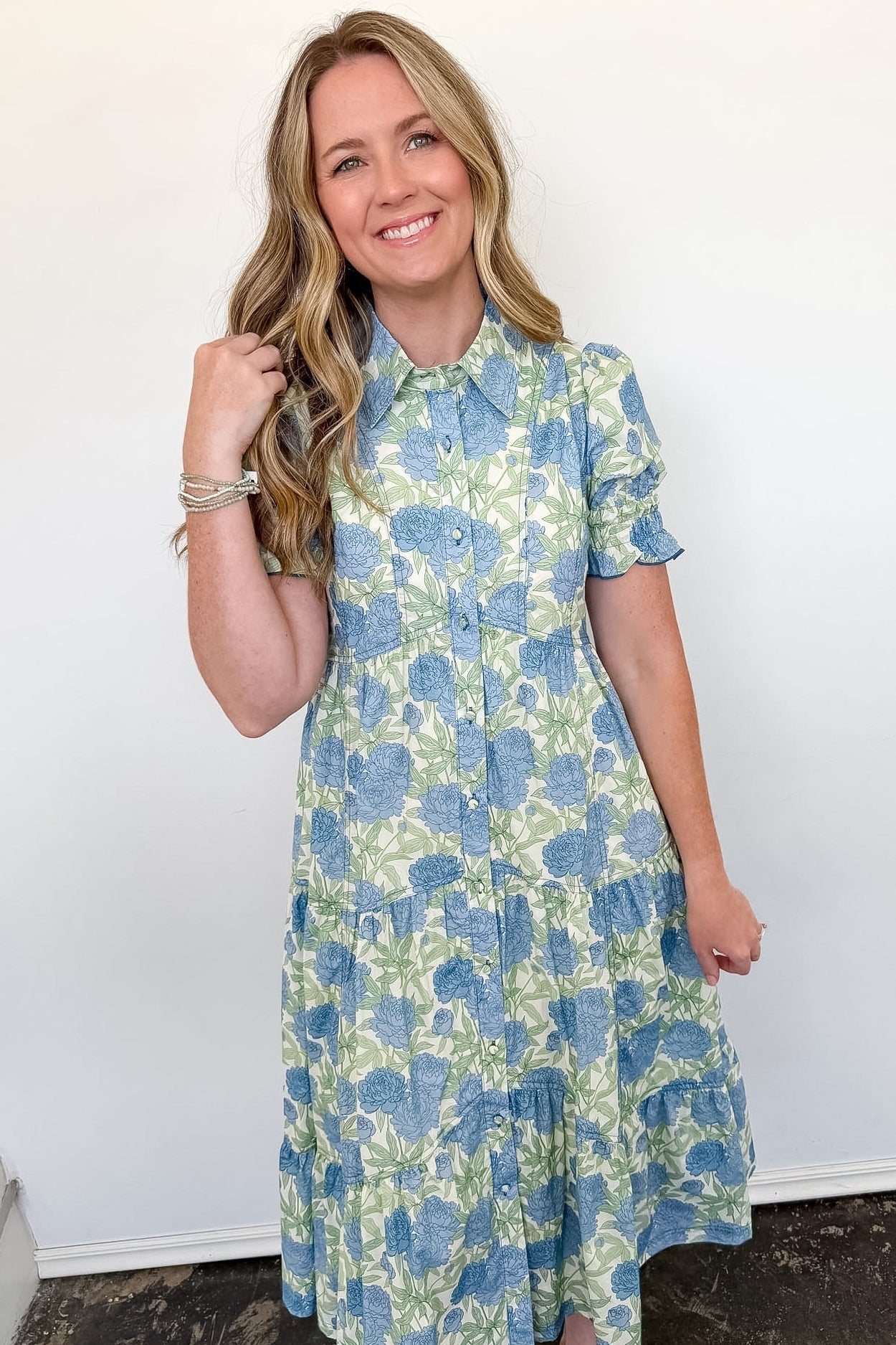 Woman wearing a blue and green floral dress against a white wall.
