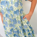 Person wearing a blue and green floral dress against a white wall.