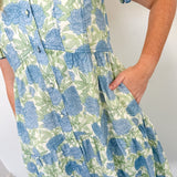 Person wearing a blue and green floral dress against a white wall.