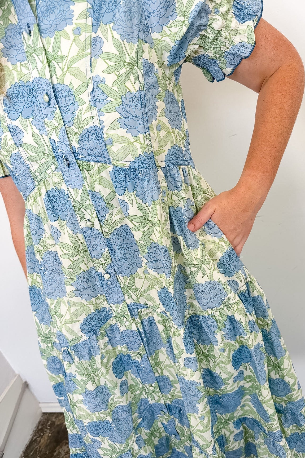Person wearing a blue and green floral dress against a white wall.