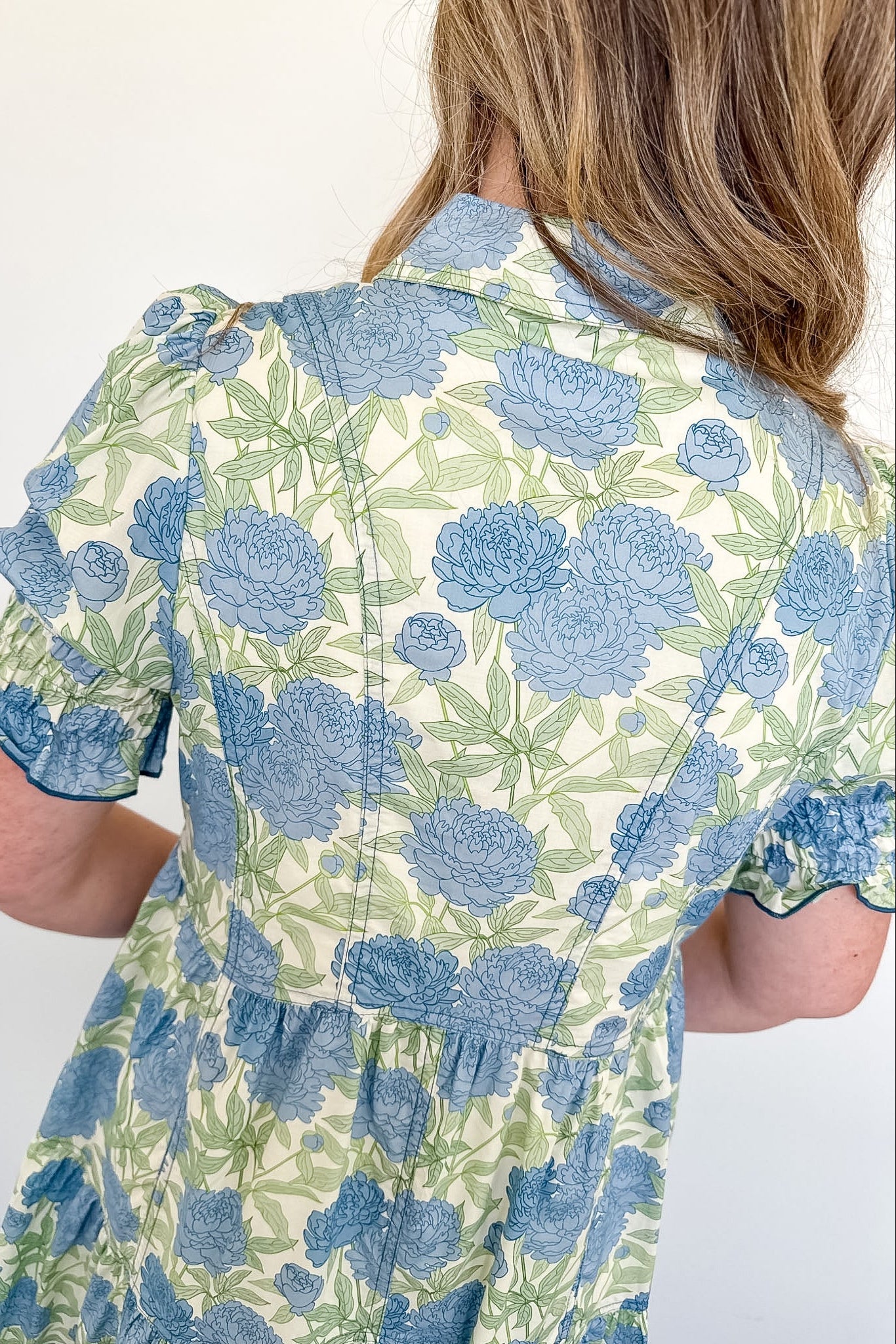 Person wearing a floral shirt with blue and green flowers on a white background