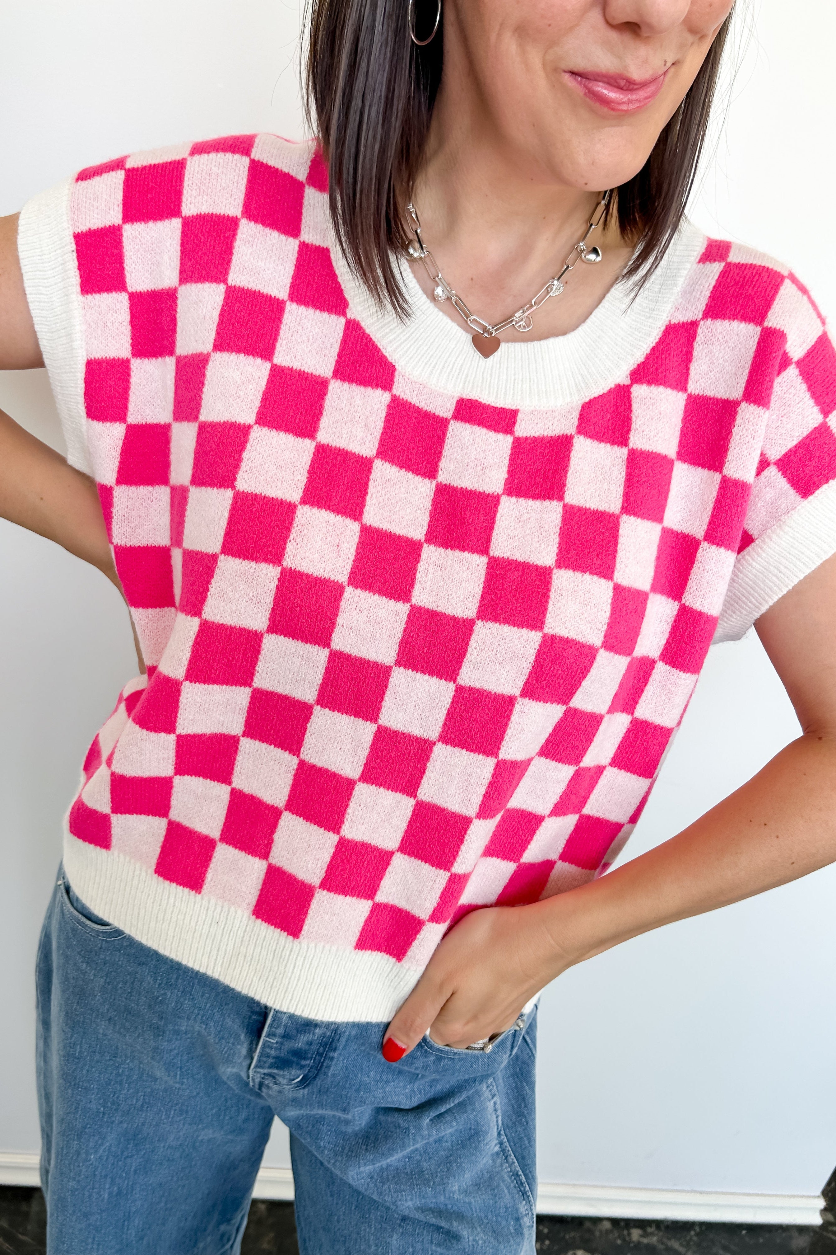 Person wearing a pink and white checkered top with blue jeans against a white background