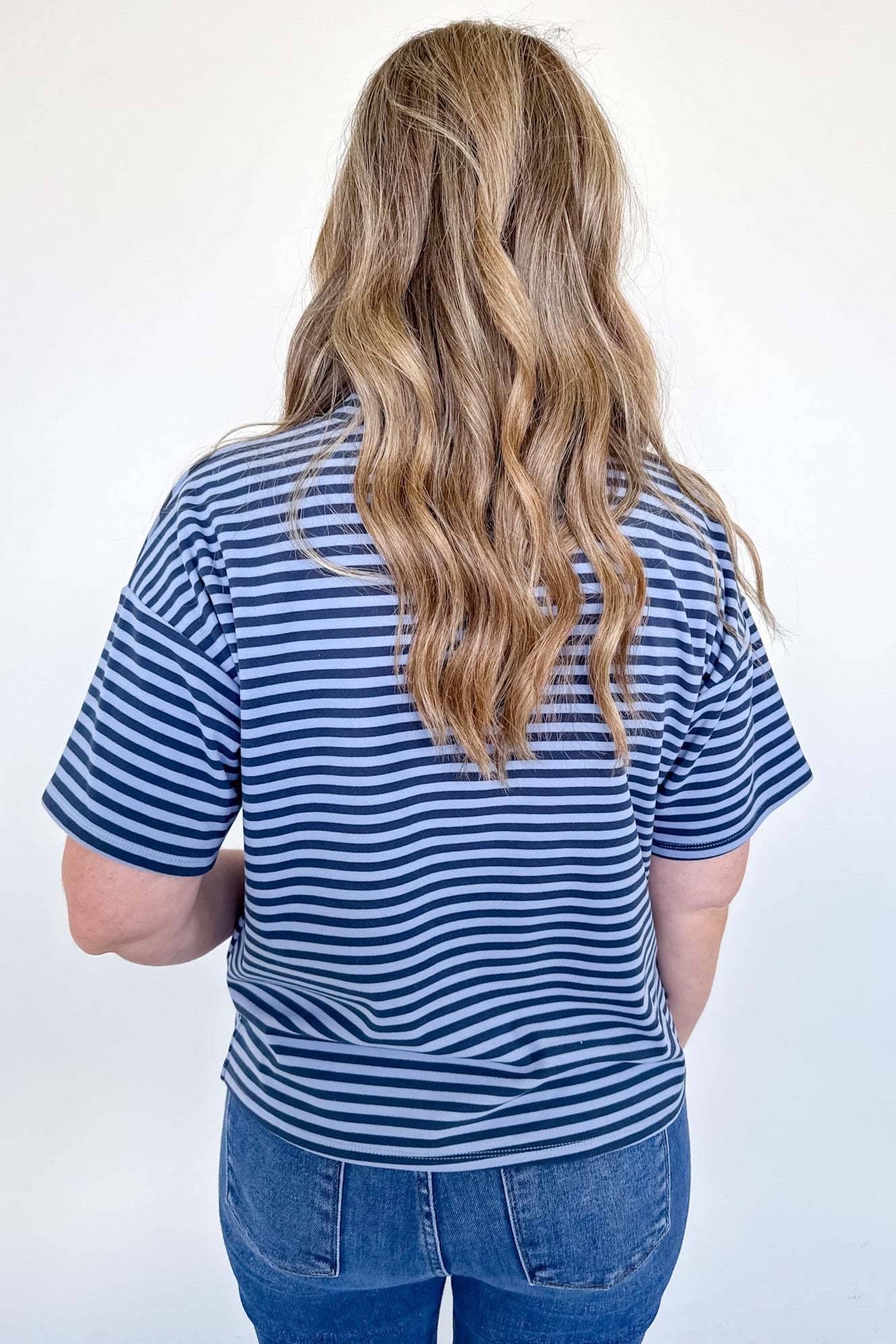 Person wearing a blue and white striped shirt and jeans against a white background