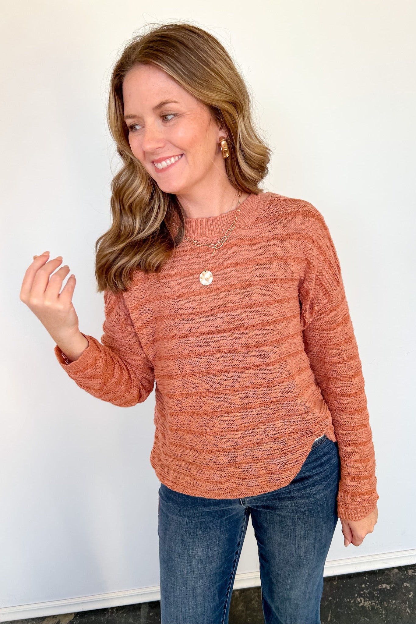 Woman wearing striped orange sweater against a white wall with necklace on.