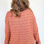 Woman facing a white wall with orange striped sweater on.