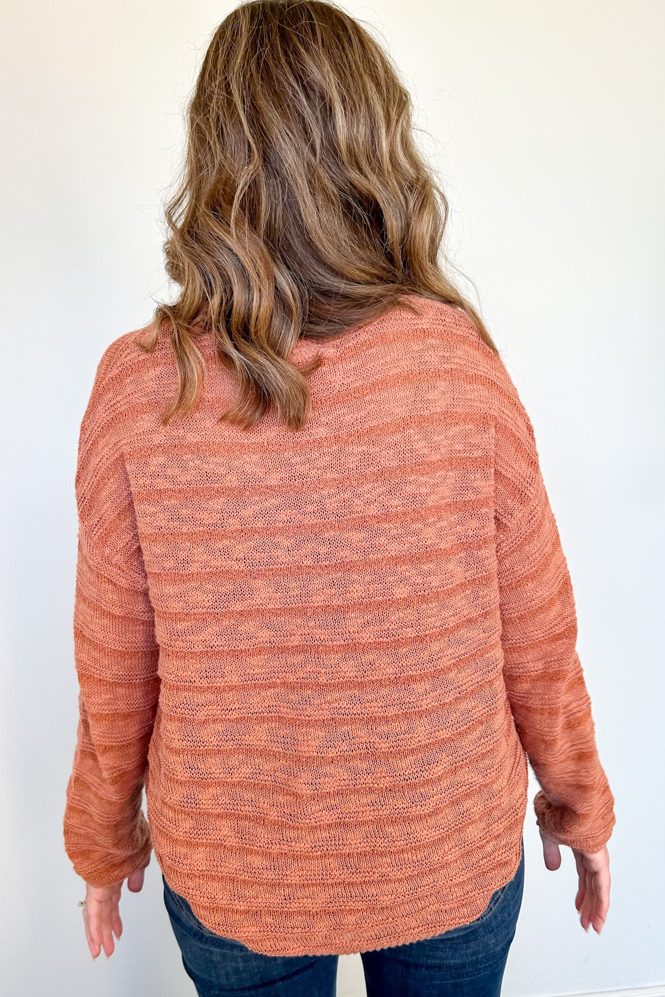 Woman facing a white wall with orange striped sweater on.