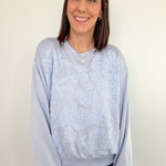 Woman wearing a light blue tie-dye sweatshirt and jeans against a white wall.