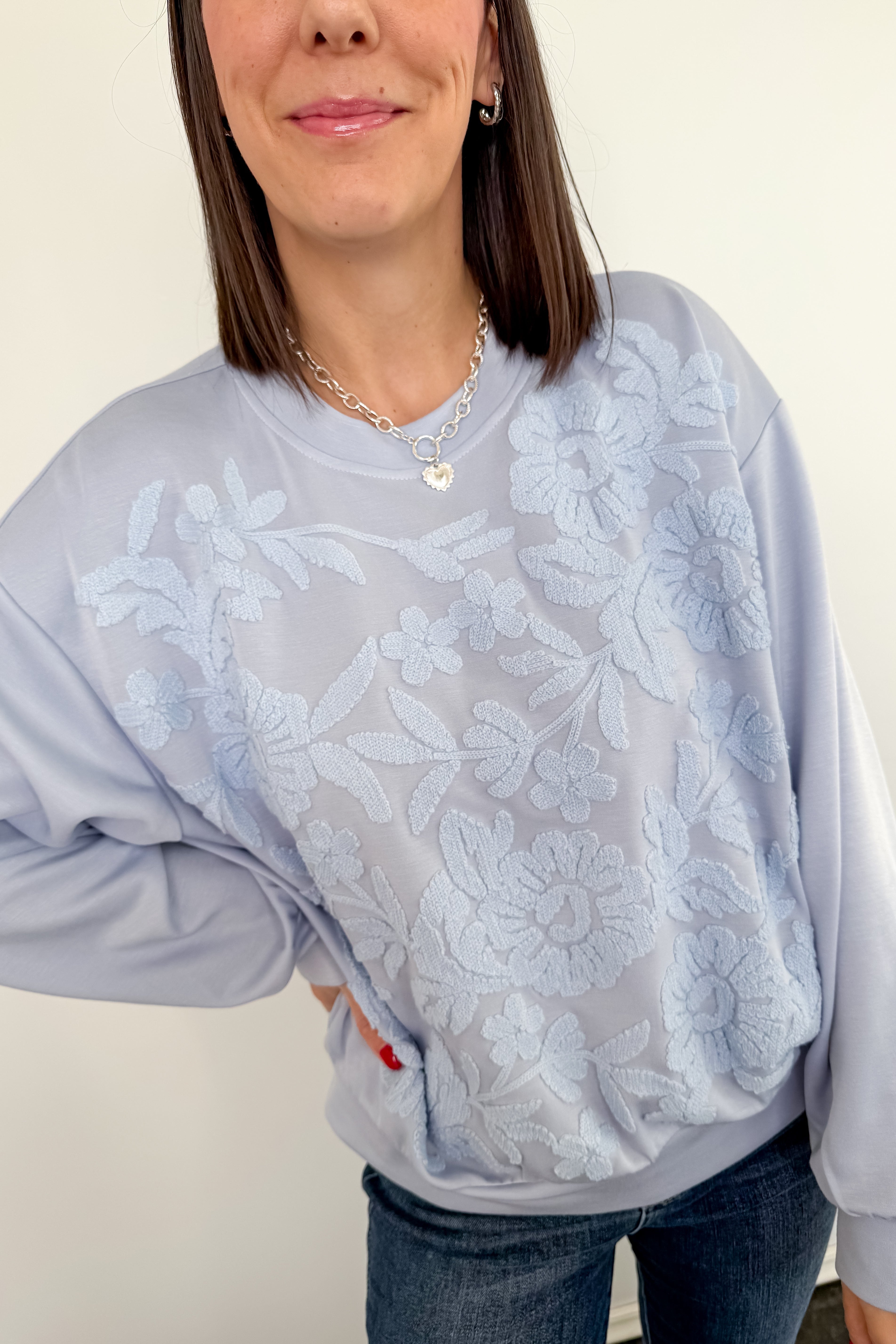Person wearing a light gray sweatshirt with floral lace overlay on a plain background