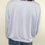 Person wearing a light blue sweater and jeans against a plain background