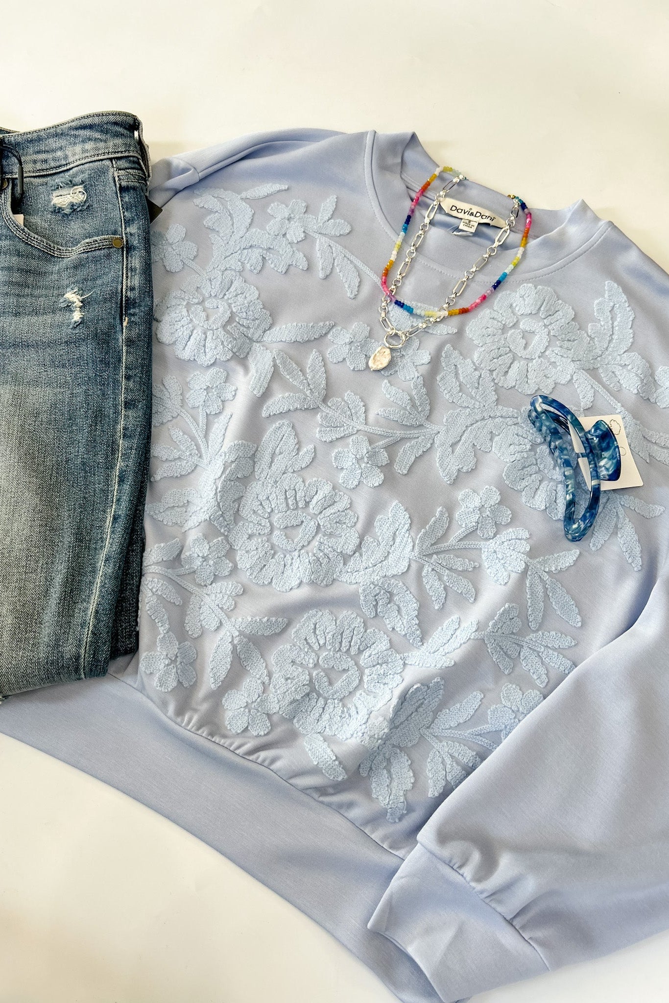 Light blue lace top with jeans and accessories on a white surface