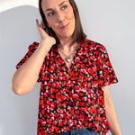 Woman wearing a red and black patterned blouse and blue jeans against a light gray background