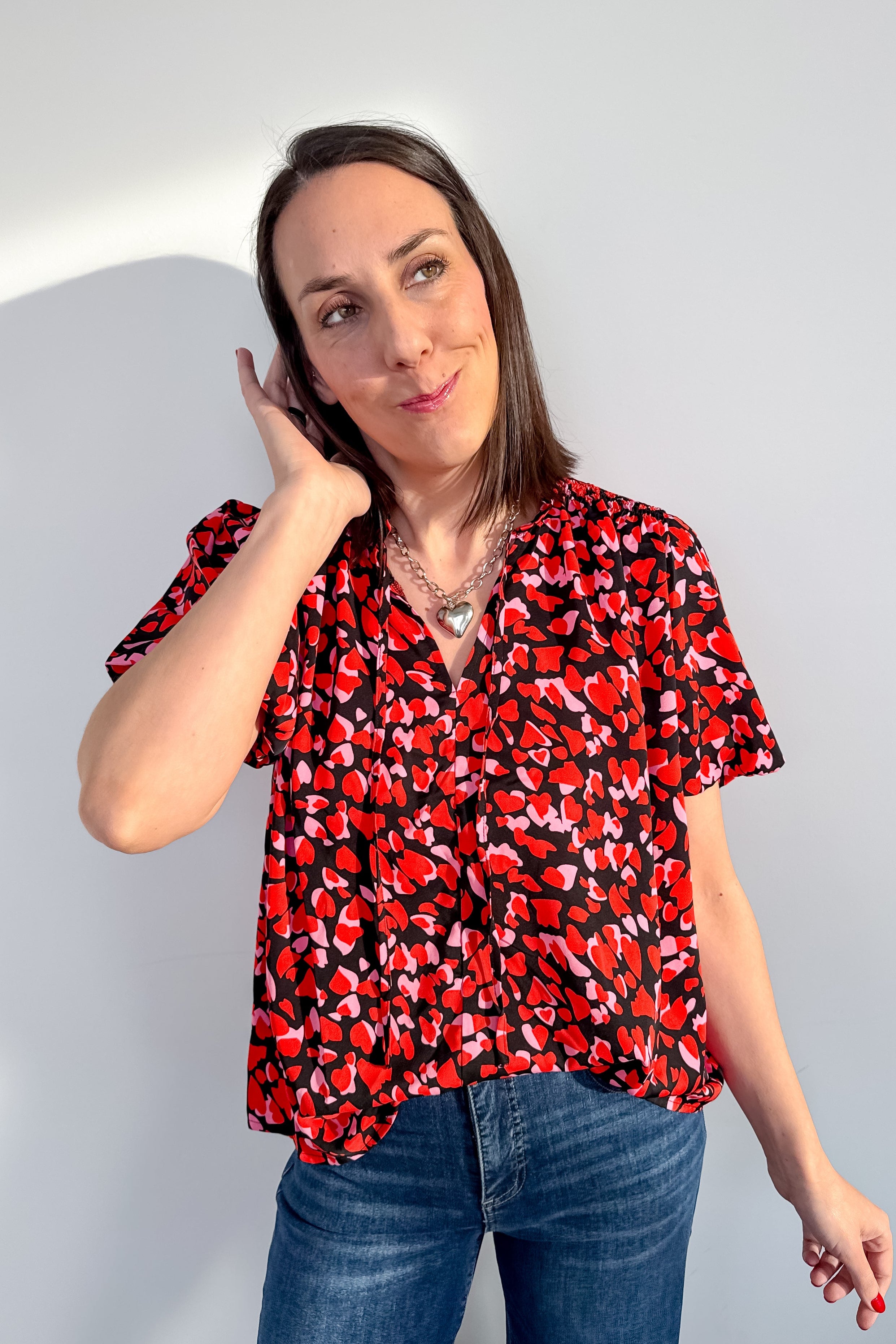 Woman wearing a red and black patterned blouse and blue jeans against a light gray background